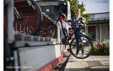 Mädchen läd ihr Rad auf den Anhänger am Fahrrradbus auf.